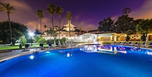 Ein Pool mit Liegestühlen, Palmen und ein Gebäude mit Kuppeldach im Hintergrund.