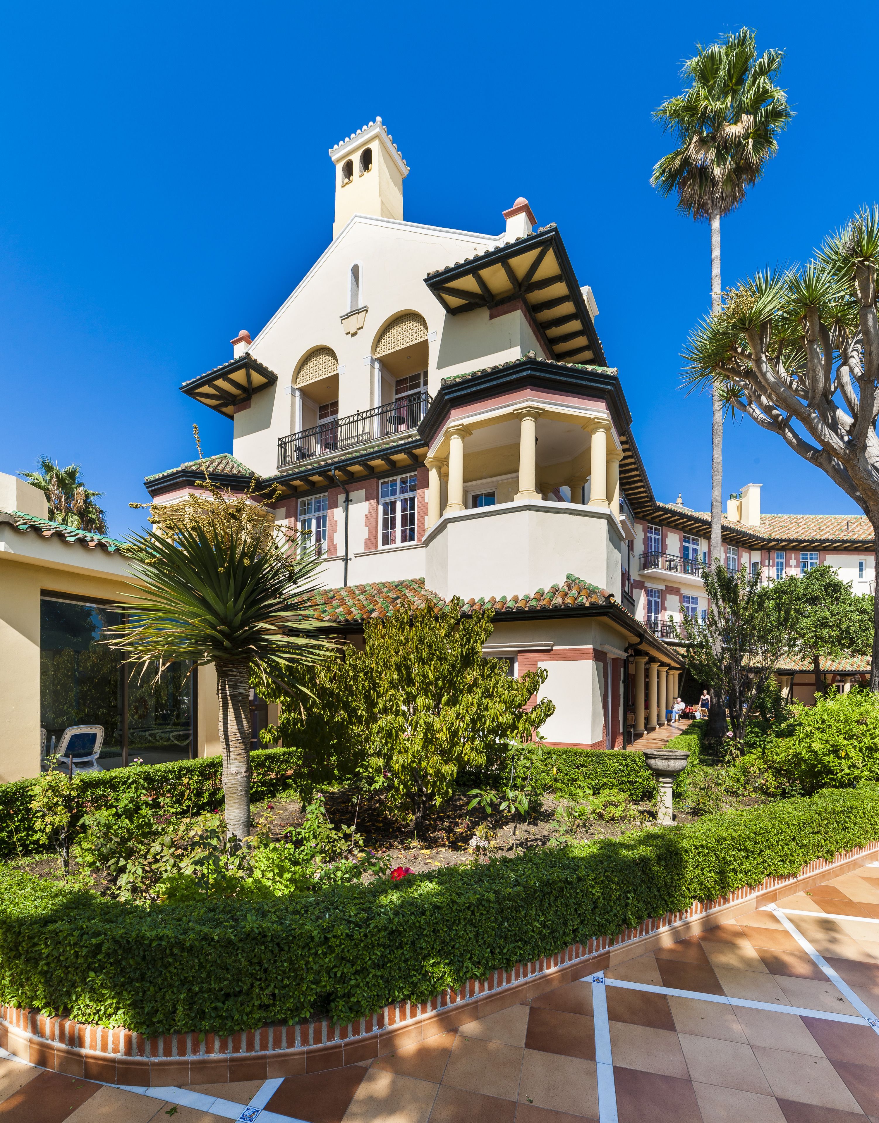 A multi-story building with a balcony, surrounded by lush greenery and palm trees.