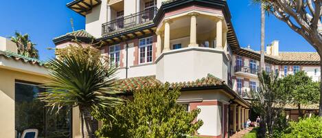 A multi-story building with a balcony, surrounded by lush greenery and palm trees.