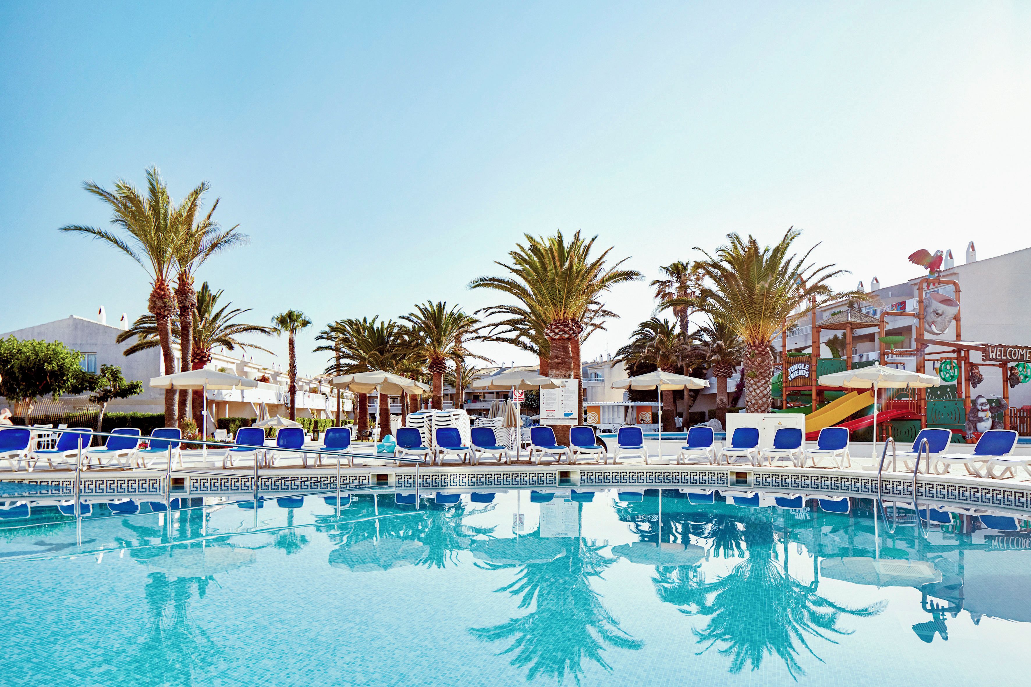 A swimming pool with lounge chairs and palm trees.
