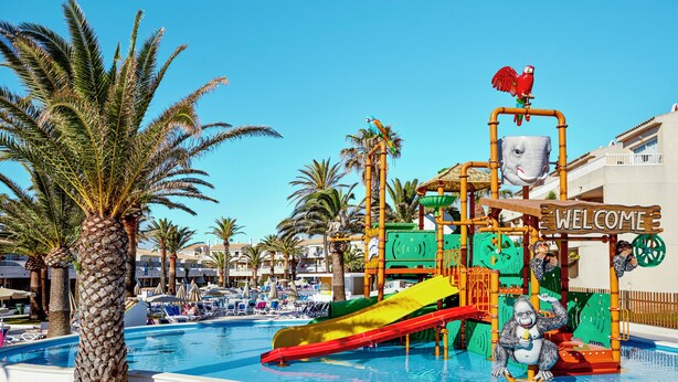 A pool area with a water slide, palm trees, and a 'Welcome' sign. - Hotel Globales Los Delfines (Ciutadella de Menorca)