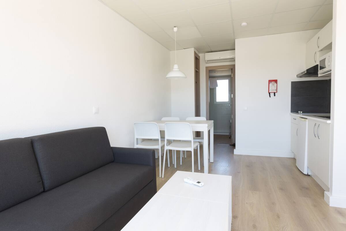 Ein modernes Wohnzimmer mit einem dunkelgrauen Sofa, einem weißen Couchtisch und einem Essbereich mit weißen Stühlen und einem Tisch.