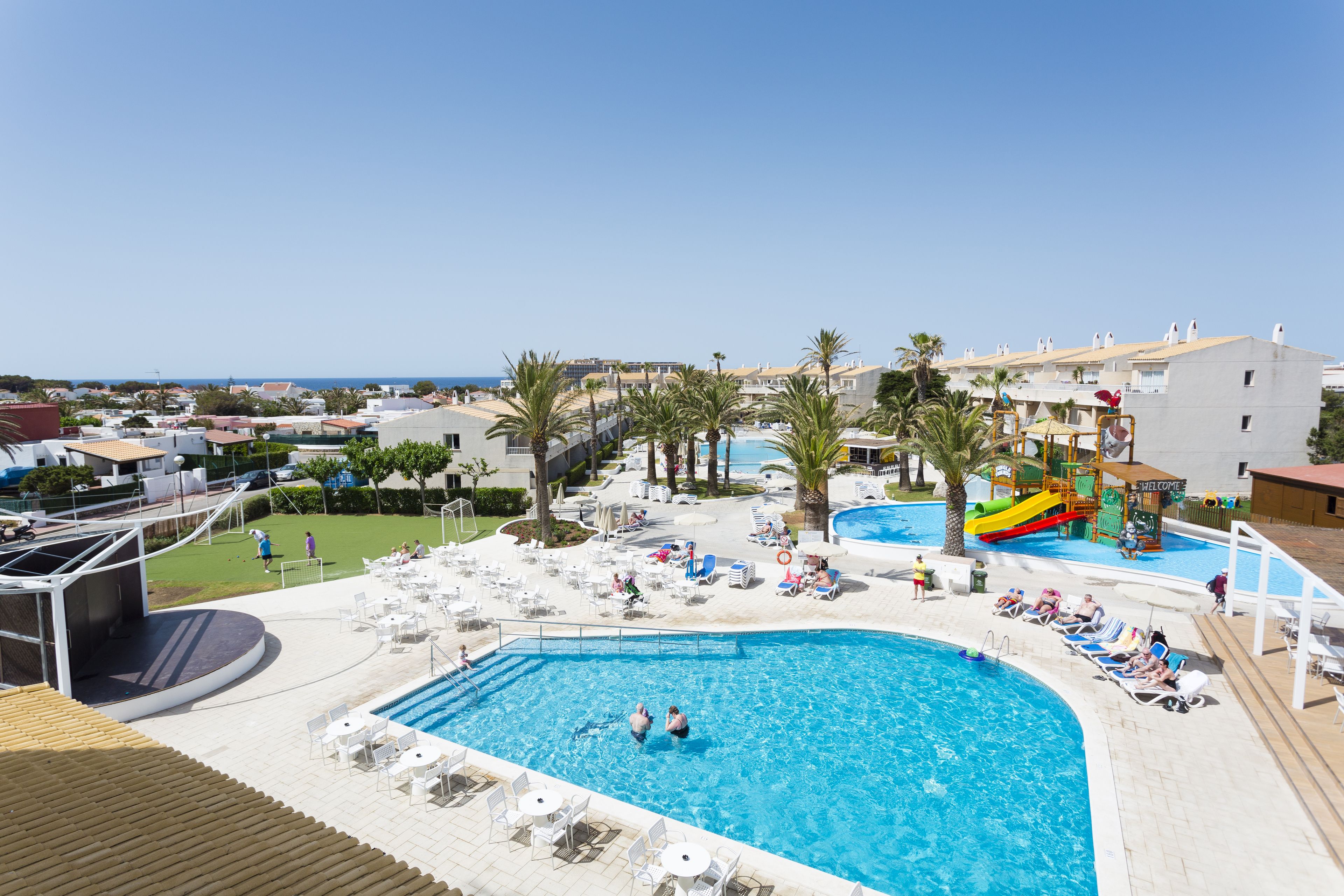 A resort pool area with a large pool, lounge chairs, and a water slide.