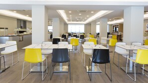 Eine großzügige Cafeteria mit hohen Tischen und Stühlen, viel Licht und einem klaren, modernen Design.