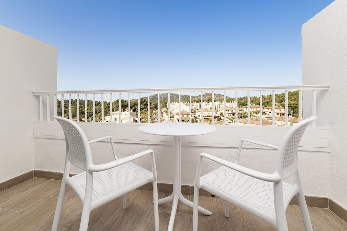 Un balcon avec deux chaises blanches et une petite table ronde, offrant une vue panoramique sur les bâtiments et la verdure.