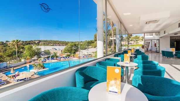 Un balcón de hotel con vista a la piscina, sillas color turquesa y cielo despejado.