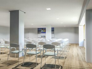 A conference room with rows of white chairs, a wooden floor, and a large pillar. - Globales Mimosa (Calvia)