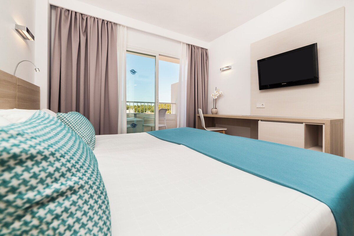 A modern hotel room with a large bed, a desk, and a TV.