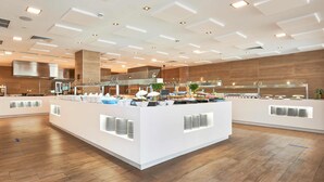 Un área de buffet moderna con mostradores blancos, suelo de madera y una cocina al fondo.