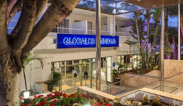 A hotel with a glass facade, outdoor seating area, and a sign reading "GLOBALES MEXICO". - Globales Mimosa (Calvia)