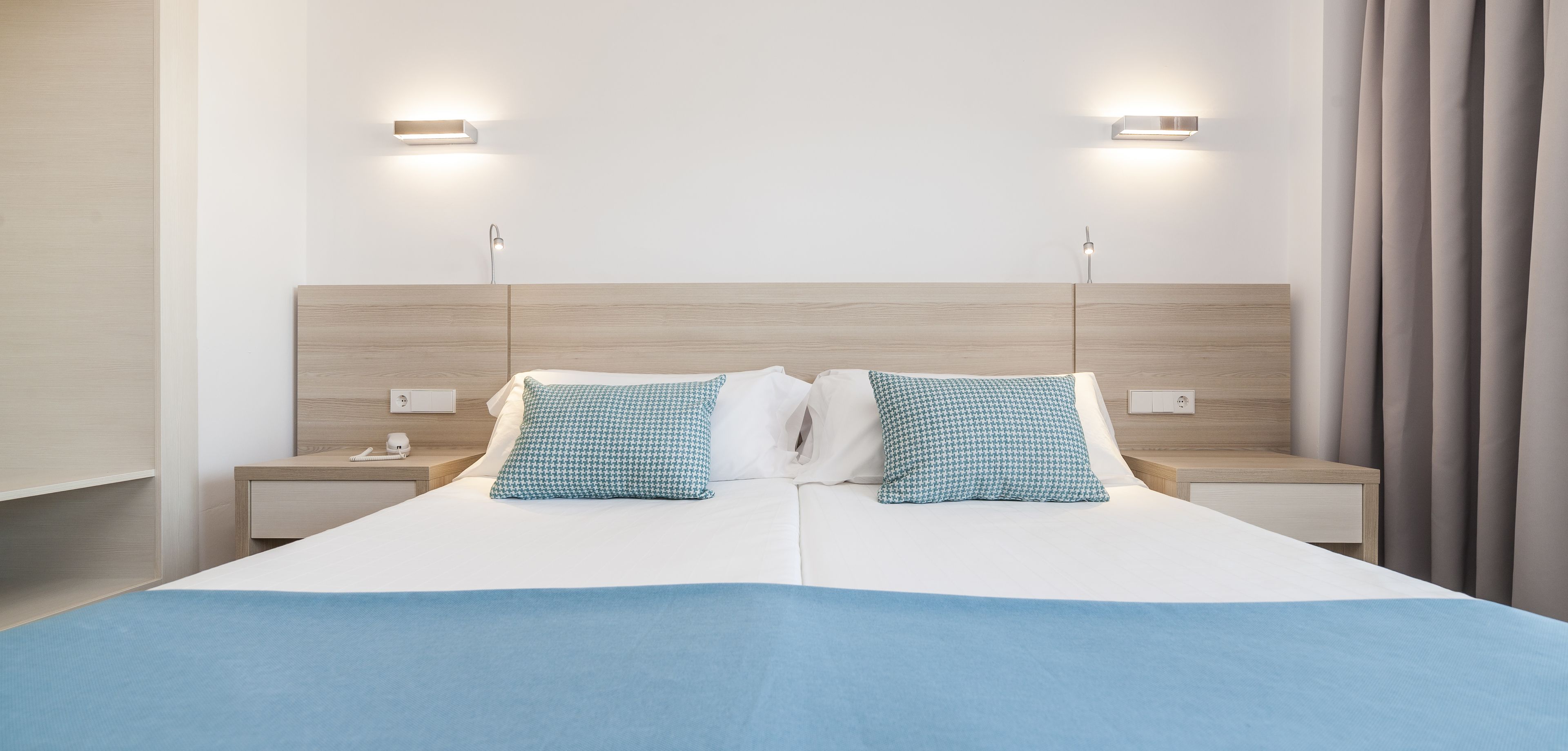 Habitación de hotel moderna con una cama grande, dos mesitas de noche e iluminación en la pared.