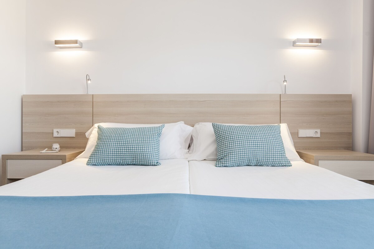 A modern hotel room with a large bed, two bedside tables, and wall-mounted lighting.