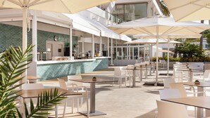 Un área de café al aire libre con mesas y sillas, piscina y bar.