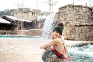 A person in a red patterned swimsuit leaning on a stone wall by a hot tub with a waterfall in the background.