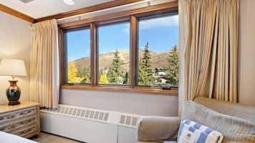 A hotel room with a large window, a radiator, a sofa, and a lamp on a dresser.