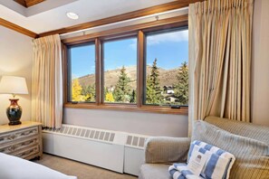 Habitación de hotel con un ventanal grande, un radiador, un sofá y una lámpara sobre una cómoda.