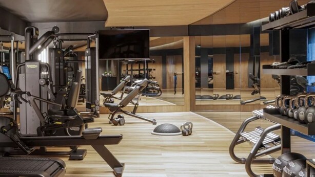 Un gimnasio moderno con diversos equipos de ejercicio, un espejo grande y una televisión.