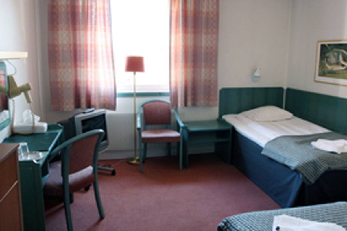Ein Zimmer mit Bett, Schreibtisch, Stuhl und einem Fenster mit Vorhängen.