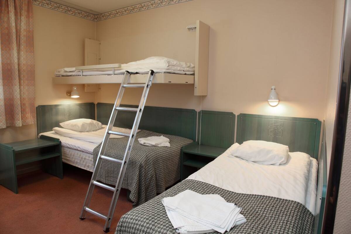 Ein Zimmer mit zwei Einzelbetten, einem Etagenbett, einer Leiter, einer Bank und einem kleinen Schrank.