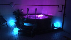 A hot tub with a ladder, surrounded by tiled flooring, and illuminated by blue and purple lights.