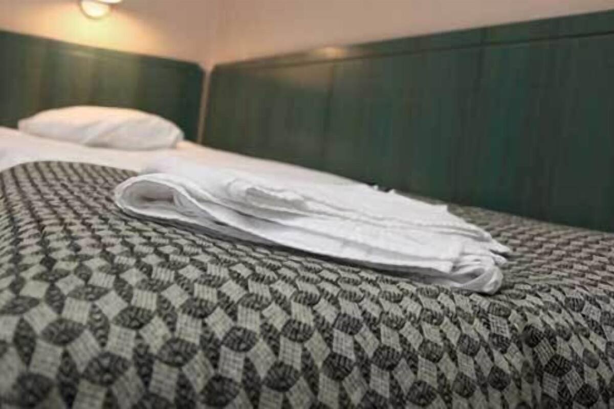Ein ordentlich bezogenes Bett mit einer gemusterten Tagesdecke und einem zusammengefalteten weißen Handtuch darauf.