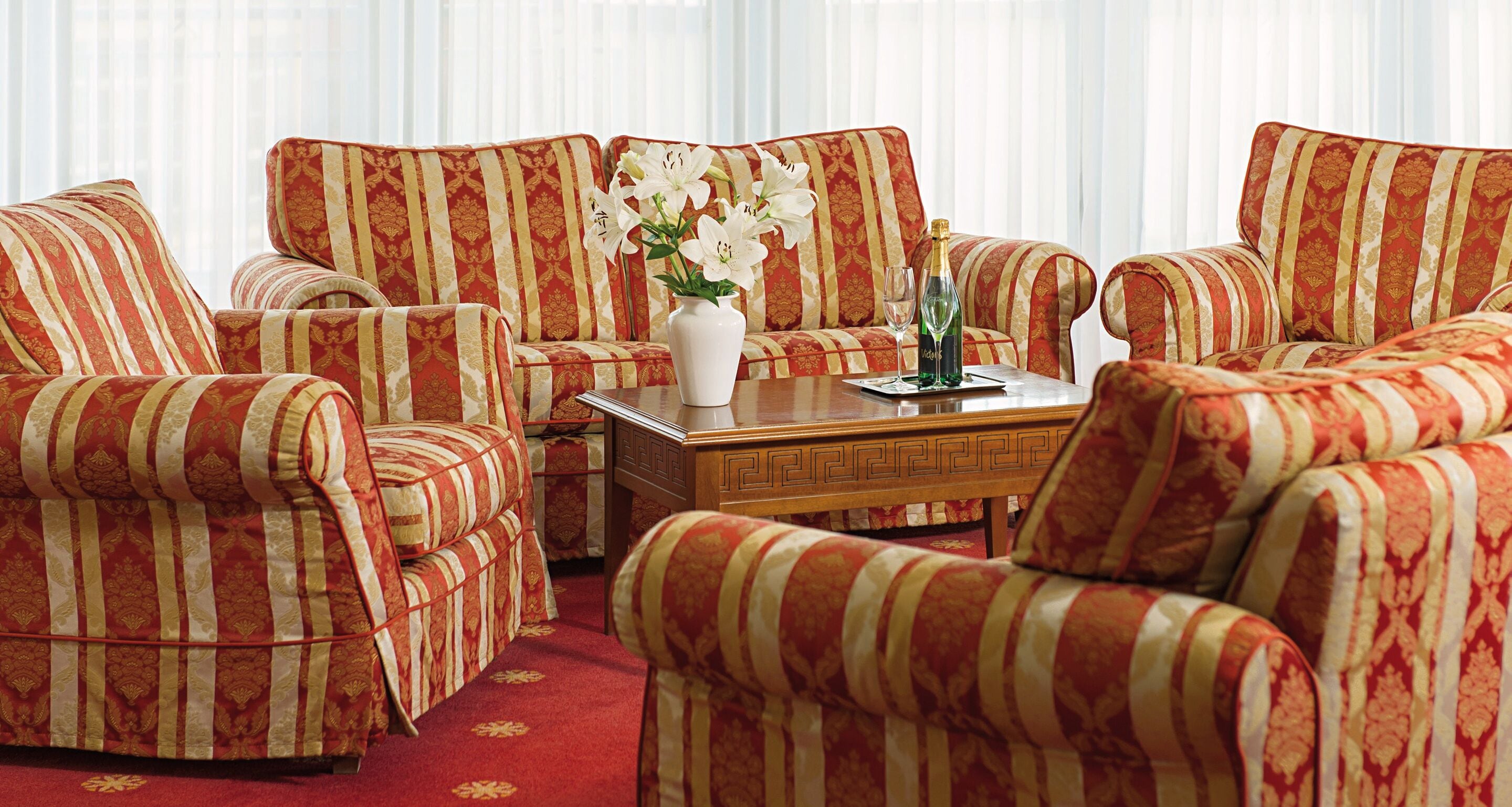 A room with striped sofas and armchairs, a wooden coffee table, and a vase with flowers.