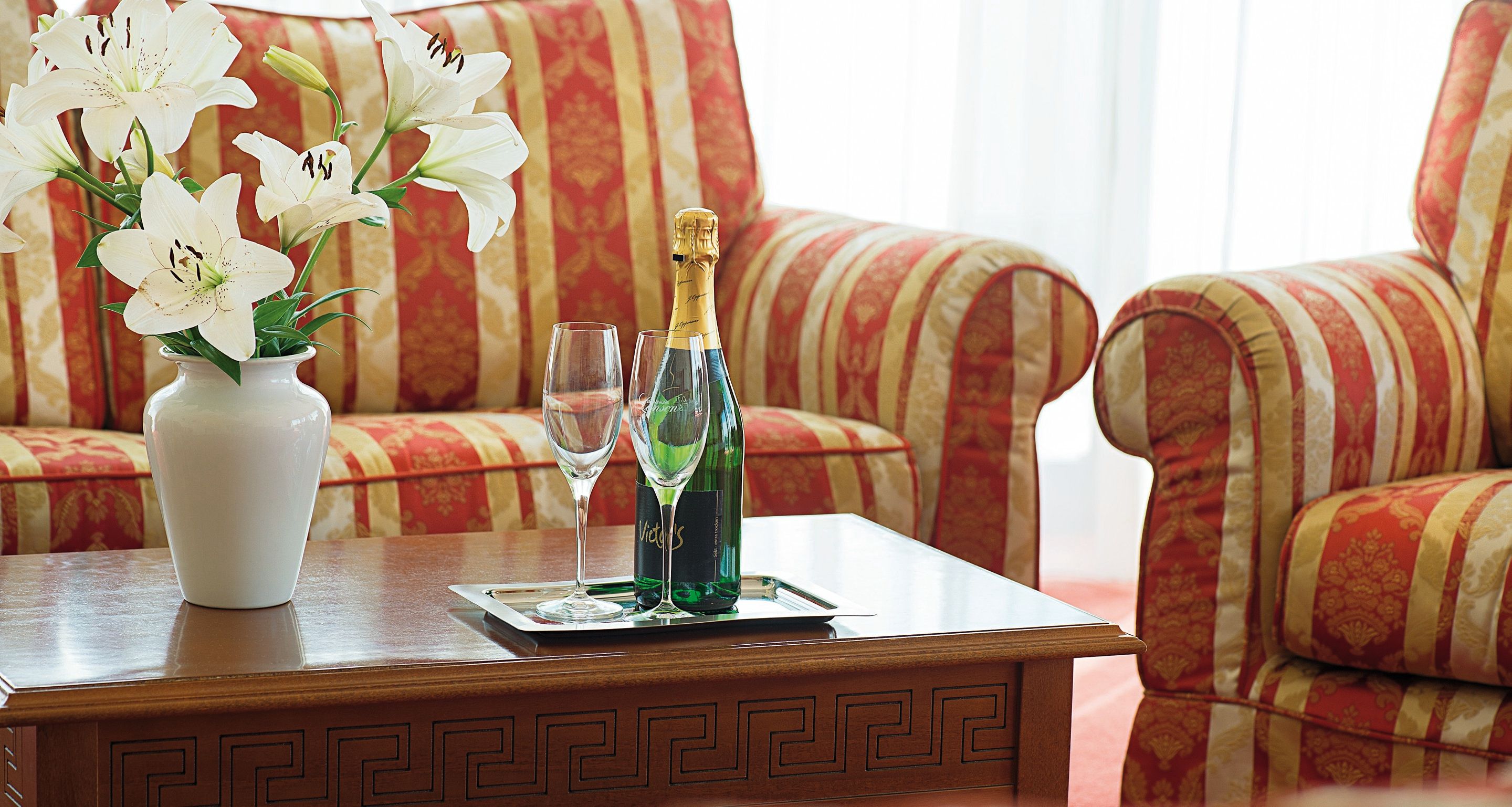 Ein Holztisch mit einer Vase weißer Lilien, zwei Weingläsern und einer Champagnerflasche.