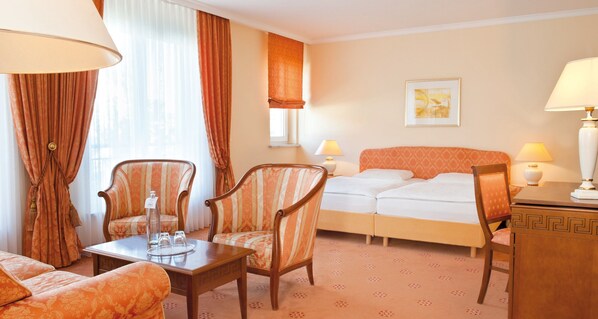 A hotel room with a bed, two armchairs, a small table with a bottle and glasses, a lamp, and a painting on the wall. - Victor's Residenz-Hotel Erfurt (Erfurt)