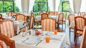 Comedor con mesas dispuestas para el desayuno, sillas a rayas y vistas al exterior con vegetación.