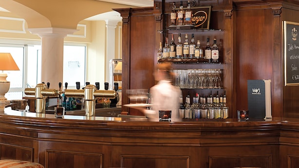 Una zona de bar con mostrador de madera, diferentes botellas de licores y un menú en una pizarra.
