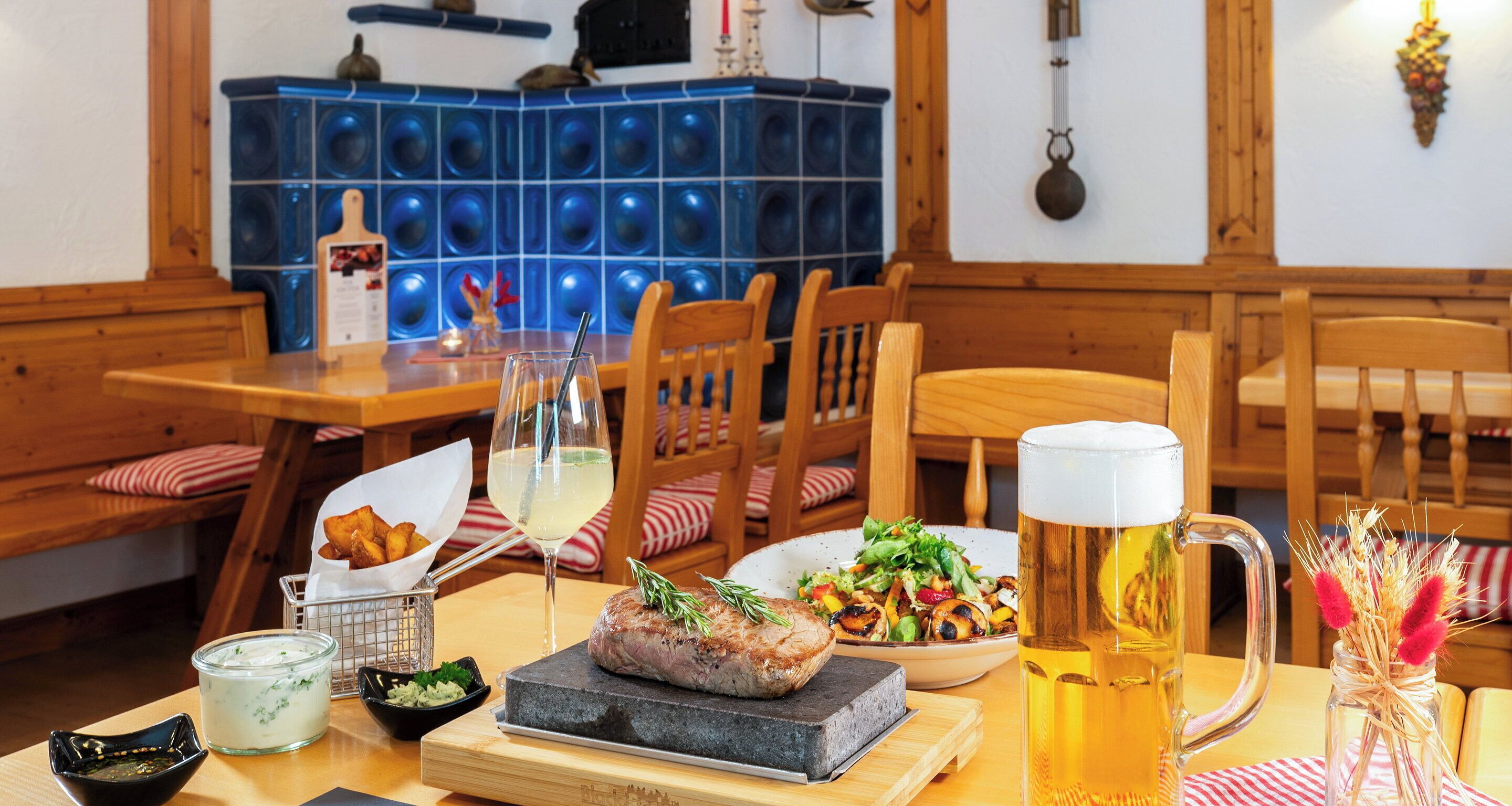A dining table with a steak, salad, beer mug, and various condiments.