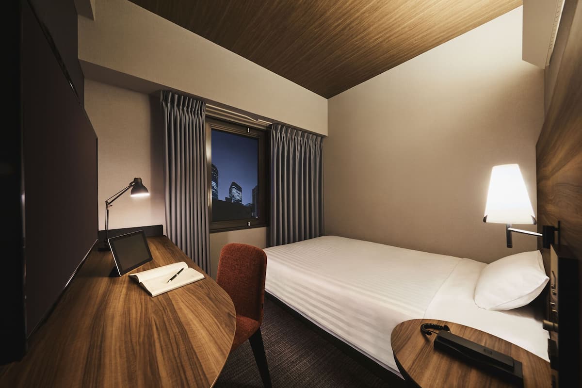 A hotel room with a bed, desk, chair, lamp, and window with curtains.