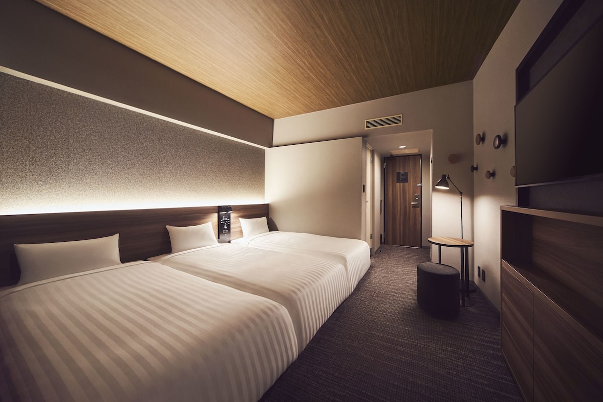 A hotel room with two beds, a wooden ceiling, a small table, and a wall-mounted TV.