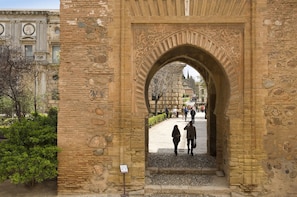 An ancient stone archway with intricate carvings, leading to a paved area with people walking. - ibis Granada (Armilla)