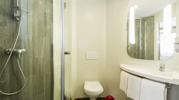 Ein modernes Badezimmer mit einer gläsernen Duschkabine, Toilette und einem Waschbecken mit Spiegel.