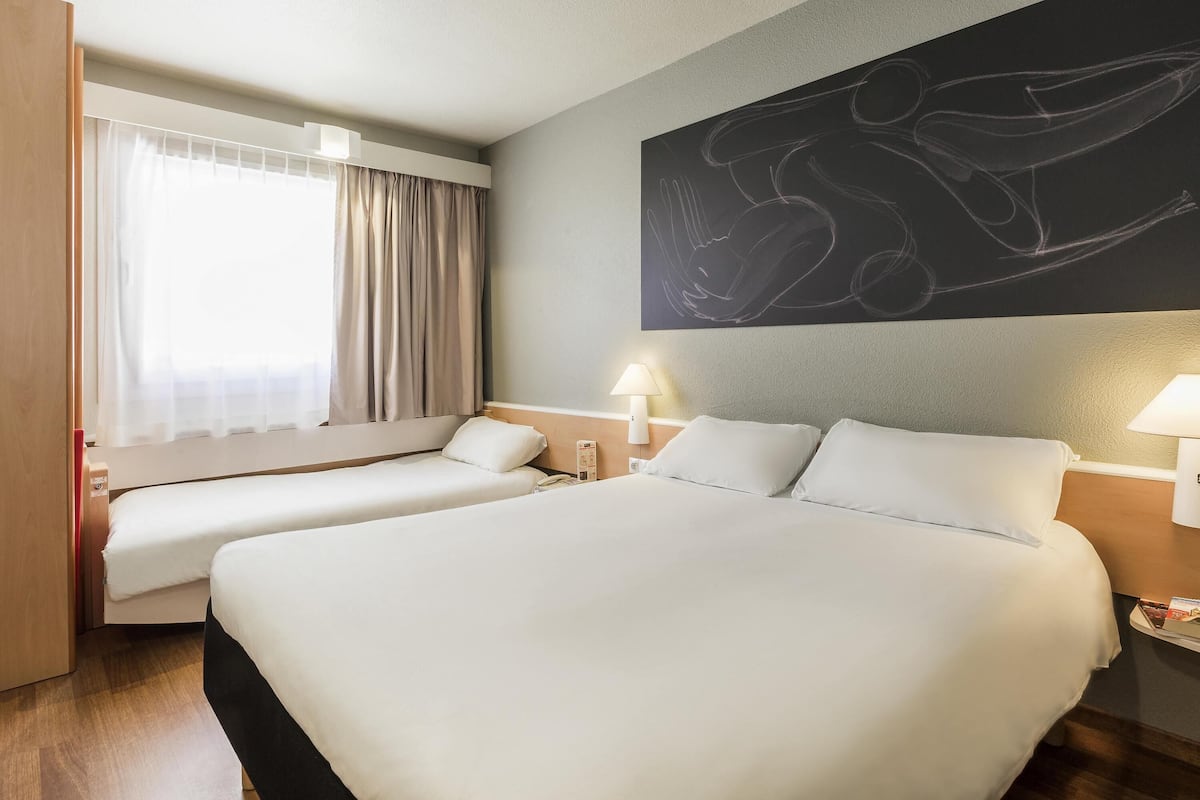 A hotel room with two beds, a large abstract painting on the wall, a window with curtains, and bedside lamps.
