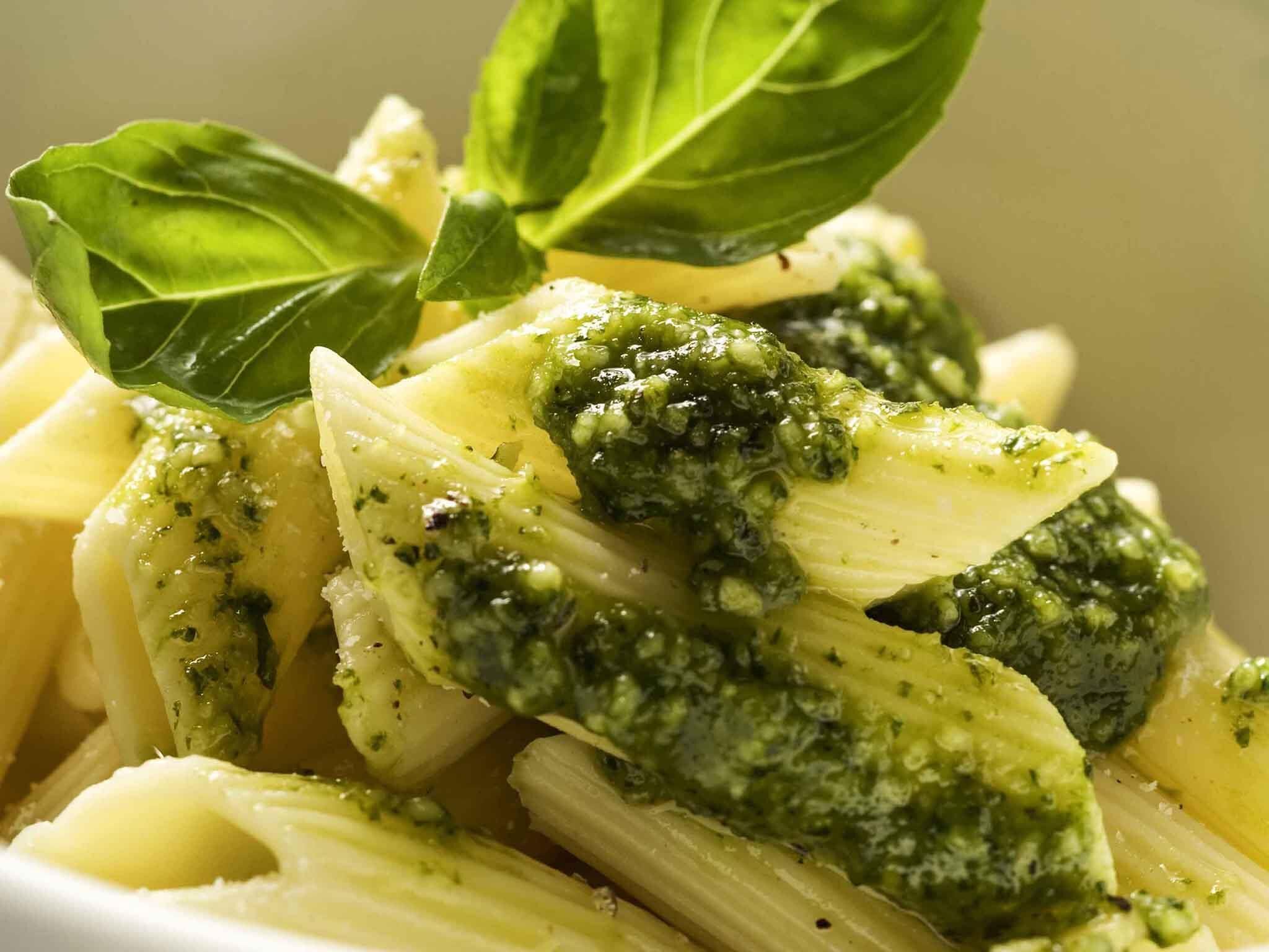 Ein Nahblick auf ein Gericht mit Pasta und grüner Sauce, garniert mit Basilikumblättern.