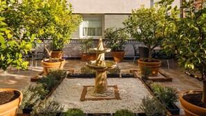 A courtyard with a central fountain, surrounded by potted plants and a tiled patio.