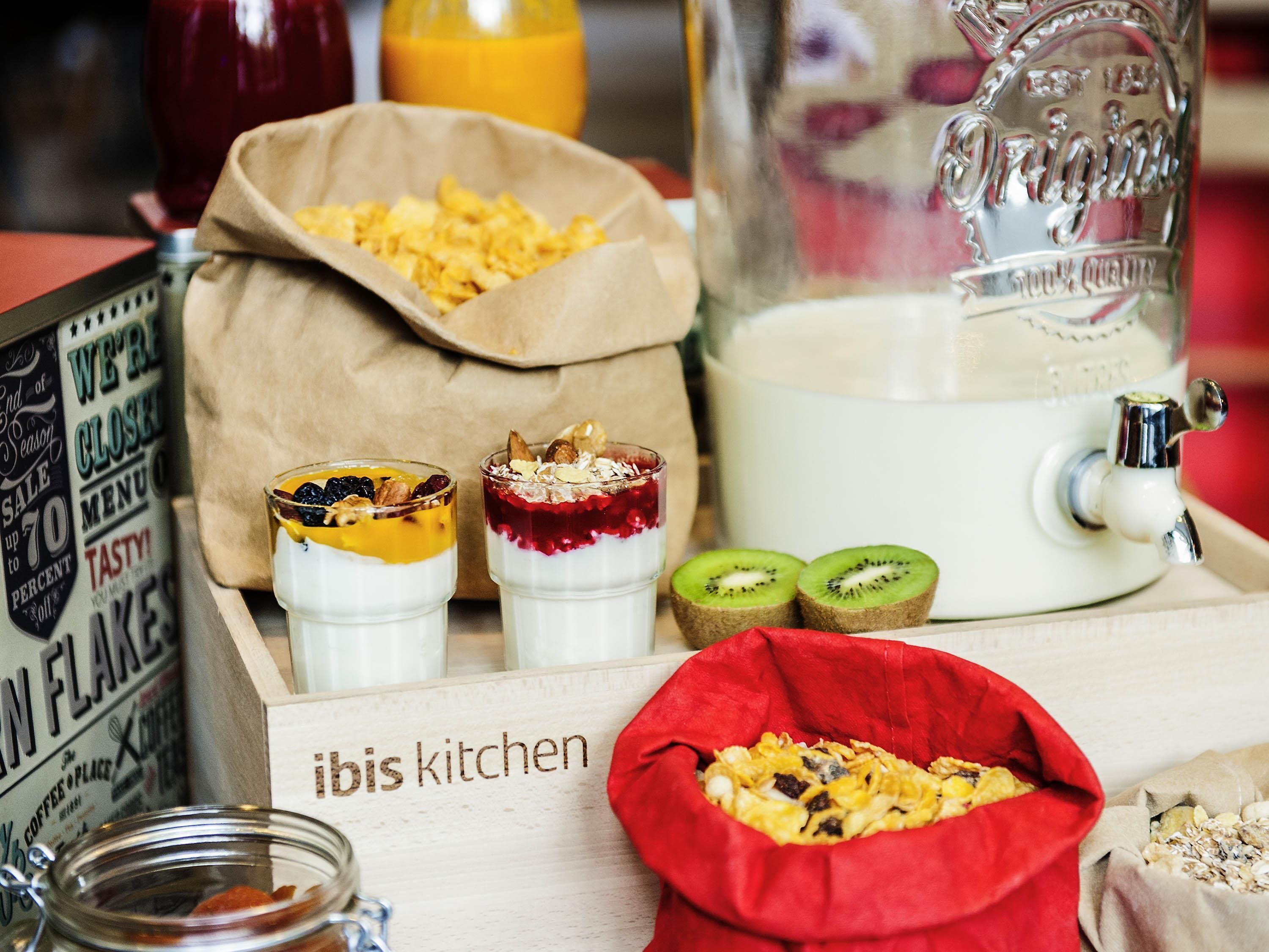 A breakfast setup with two parfaits, a pitcher of milk, and a bag of granola.