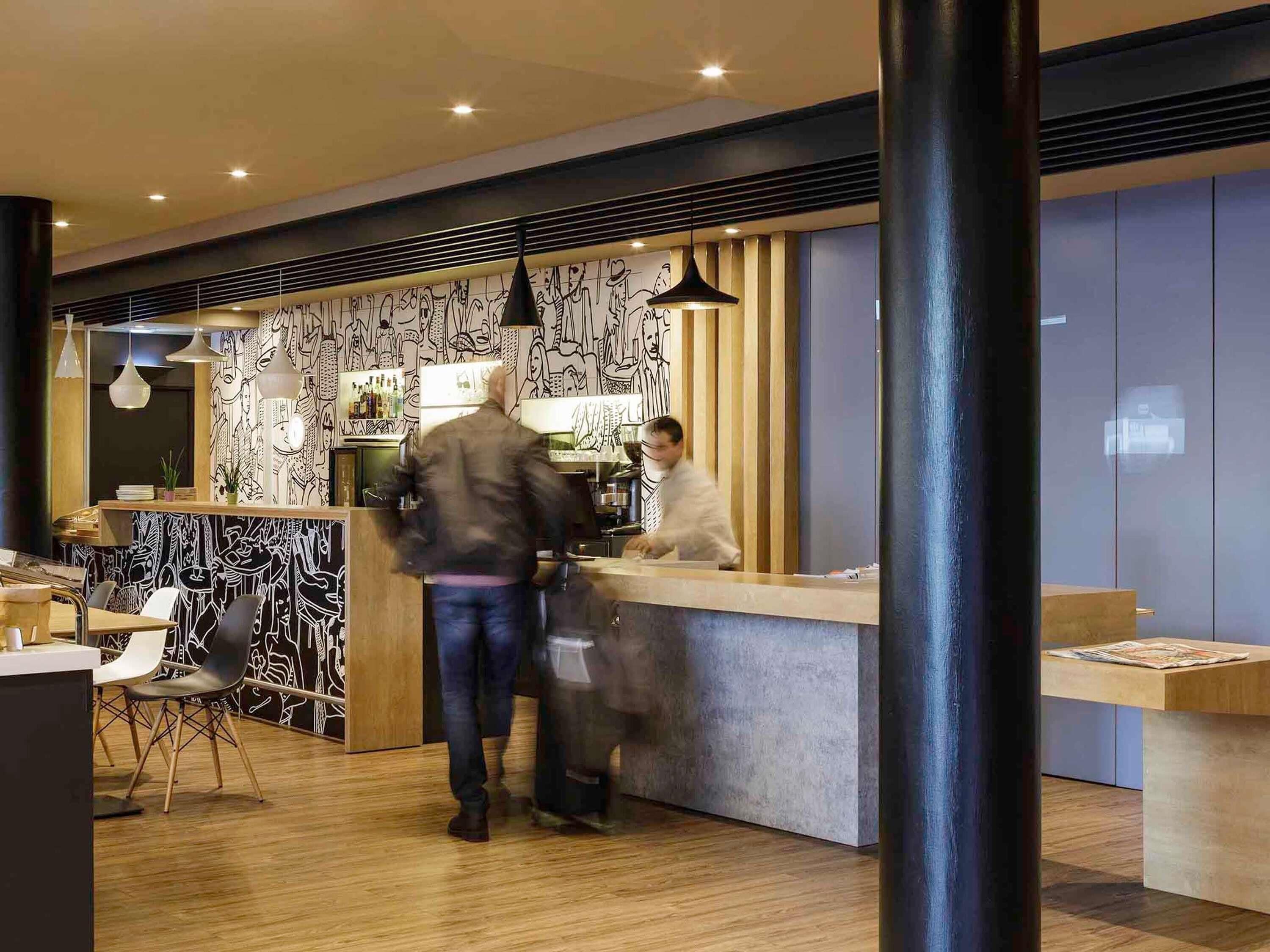 A modern interior with a bar area, wooden flooring, and a counter with a person behind it.