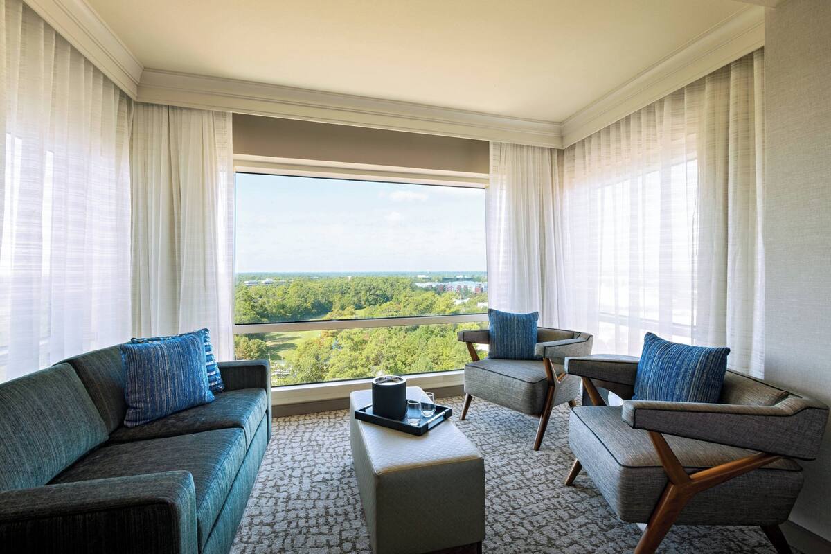 Ein modernes Hotelzimmer mit großem Fenster, einer Couch, einem Sessel und einem kleinen Tisch.