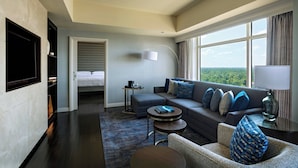 Une chambre d’hôtel moderne dotée d’une grande fenêtre offrant une vue, d’un canapé, d’un fauteuil, d ’une petite table et d’un téléviseur à écran plat.