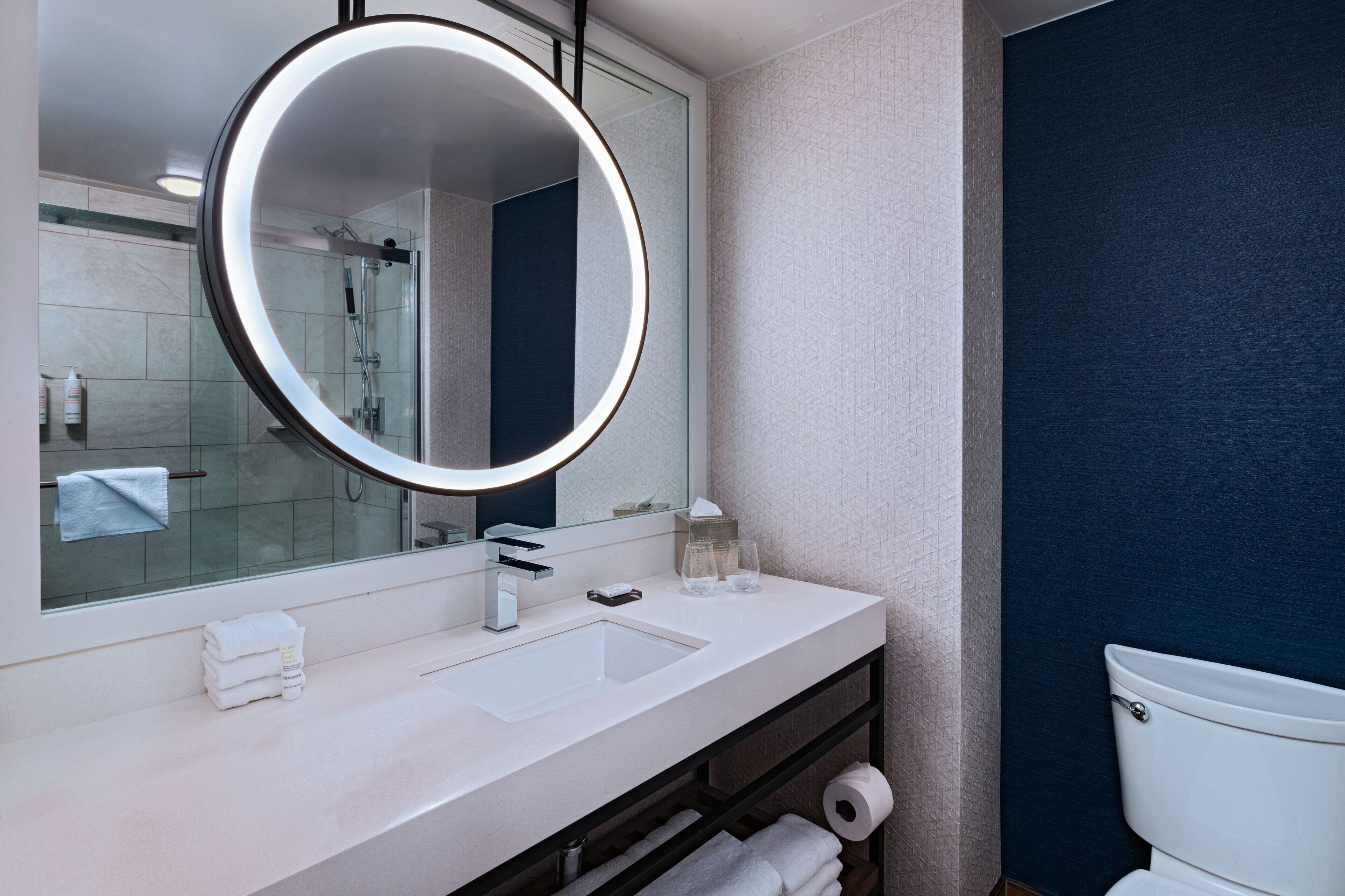 A modern bathroom with a round mirror, white sink, and a glass shower enclosure.