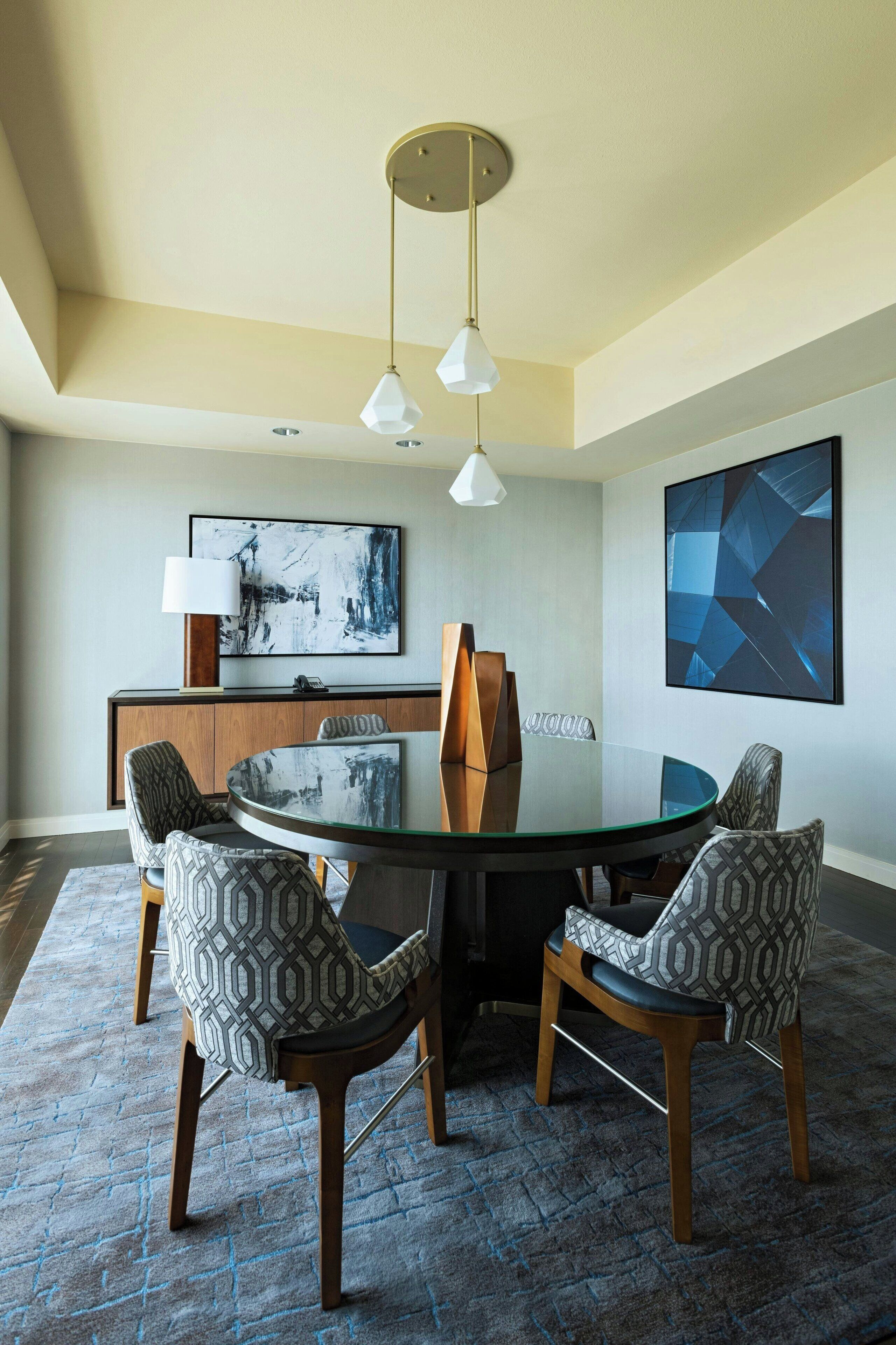 Een moderne eetruimte met een ronde glazen tafel, gestreepte stoelen, een houten kast en abstracte kunst aan de wanden.