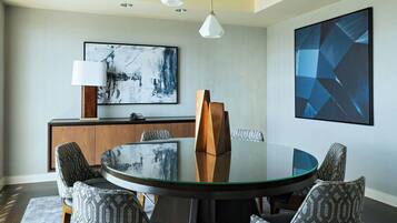 Een moderne eetruimte met een ronde glazen tafel, gestreepte stoelen, een houten kast en abstracte kunst aan de wanden.