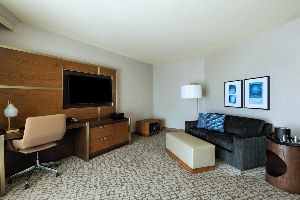 Ein Hotelzimmer mit einem Holztisch, einem Fernseher, einem Sofa, einer Lampe und gerahmten Bildern an der Wand.