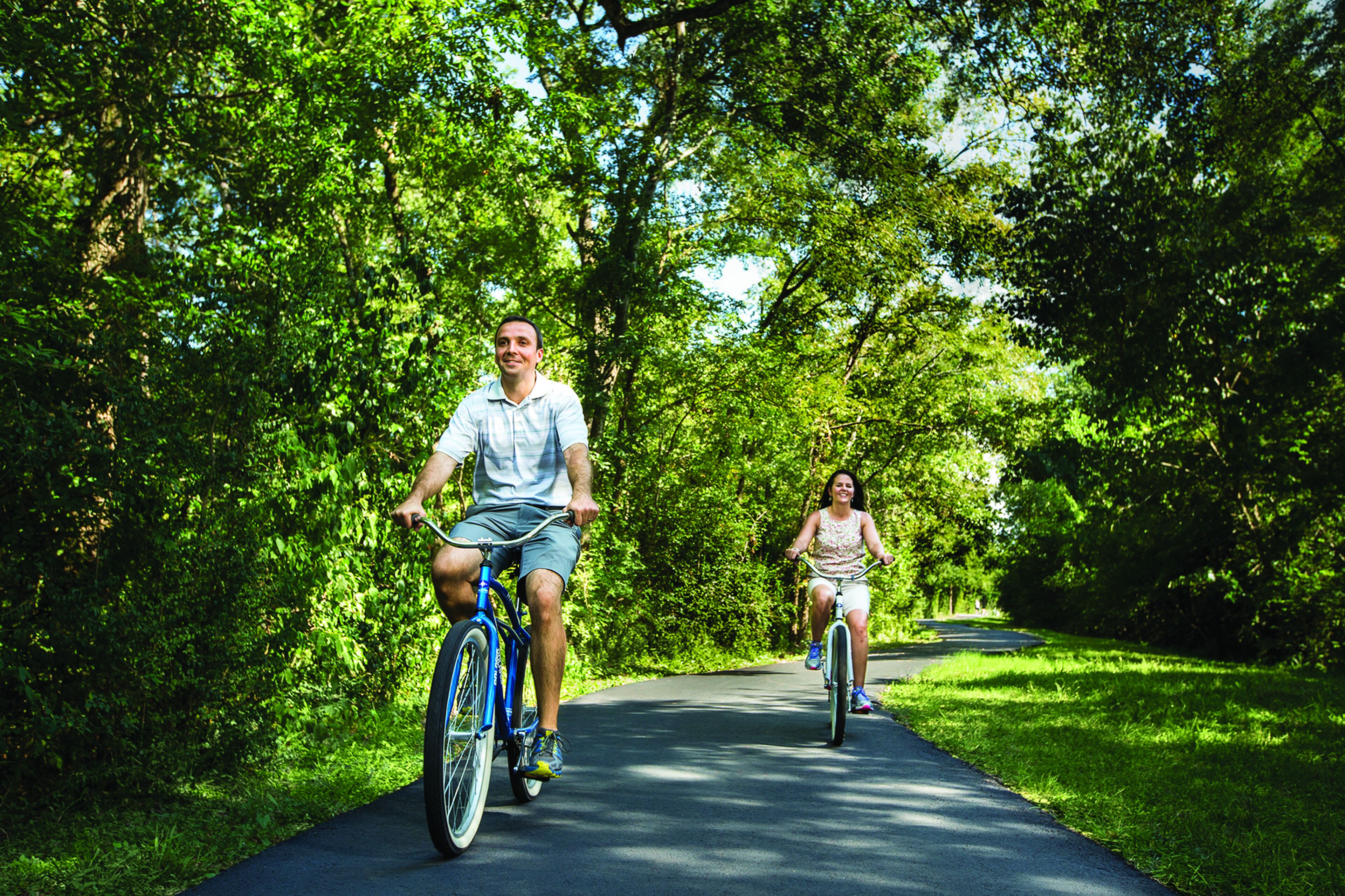 Two people riding bicycles on a paved path surrounded by lush greenery.