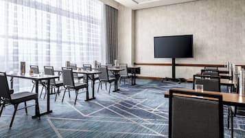 A conference room with a large screen, multiple tables, and chairs arranged for meetings.