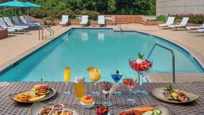 Un espace repas aménagé au bord de la piscine, avec une table dressée pour un repas, entouré de chaises longues et de la piscine elle-même.