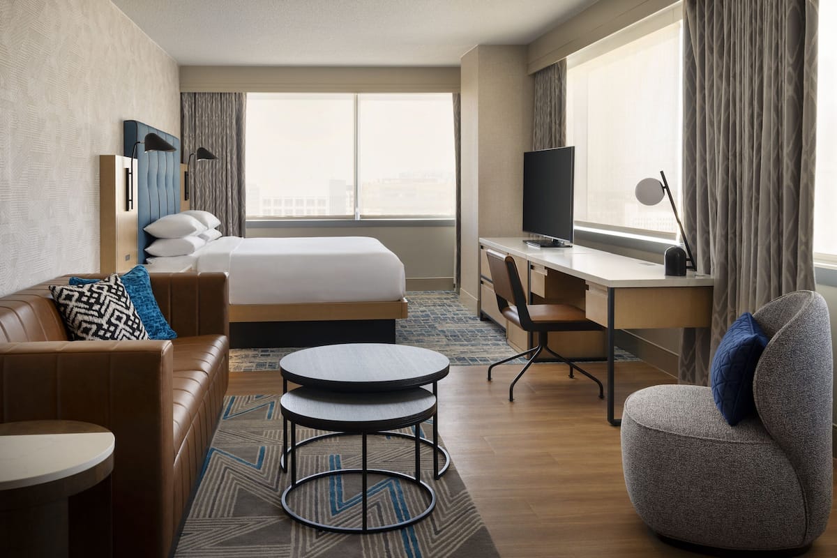 A hotel room with a bed, a desk, a chair, a sofa, and a small table.
